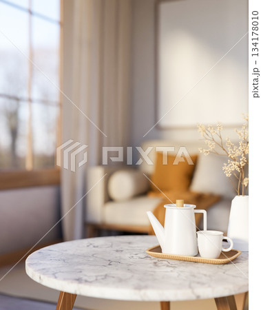 Teapot and cup on wooden tray and flower vase over round marble table across sofa in a living room. Teapot and cup on wooden tray and flower vase over round marble table across sofa in a living room. 134178010