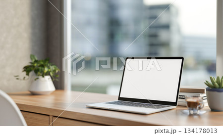 White screen laptop and coffee aside potted plant on wooden table with cityscape outside glass wall. 134178013