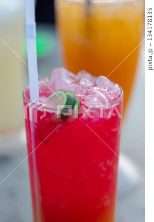 Refreshing close-up vertical shot of vibrant red summer drink garnished with lime and ice cubes on blurred background Refreshing close-up vertical shot of vibrant red summer drink garnished with lime and ice cubes on blurred background 134178135