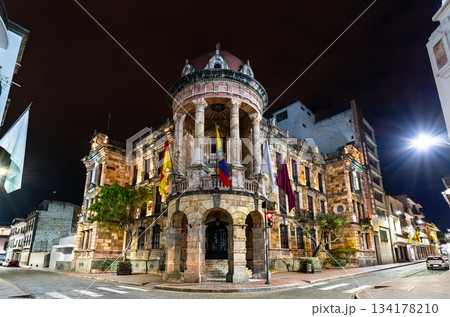 Illuminated City Hall building stands on a street corner in Cuenca, Ecuador. Historic Neoclassical structure features a stone facade and flags in the UNESCO World Heritage city center 134178210