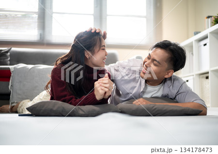 Asian man holding or touching woman's head while lying together over cushion on living room's floor. Asian man holding or touching woman's head while lying together over cushion on living room's floor. 134178473