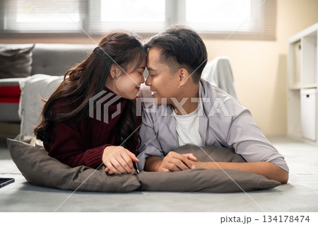 Asian man and a woman touching their head or temple together while lying on a living room's floor. Asian man and a woman touching their head or temple together while lying on a living room's floor. 134178474