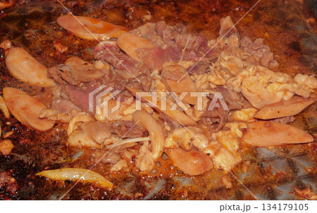 Close-up view of sizzling mixed meats and sausage cooking on a hot oiled metal griddle. 134179105