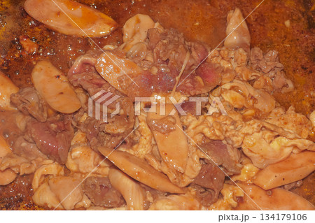 Delicious close-up of stir-fried meats and sausages cooking vigorously in spicy savory sauce on a hot grill pan. 134179106