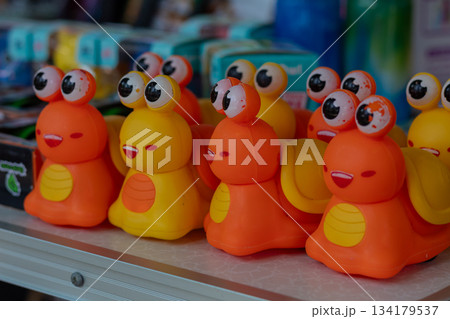 Row of bright orange and yellow plastic toy snails with funny cartoon googly eyes displayed for sale 134179537