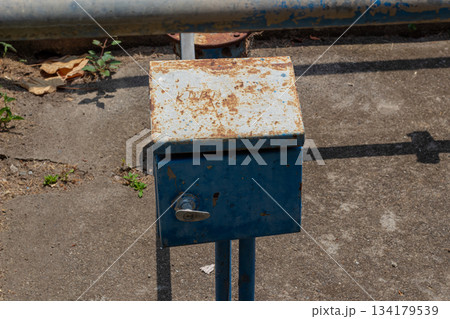 Weathered blue metal utility box with rust texture on concrete ground surface 134179539