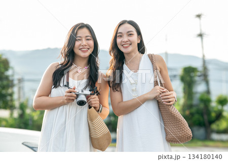 Two pretty asian women best friends standing holding bag and camera going on a trip travel together 134180140