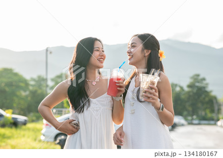 Pretty asian woman holding cup sharing drink with her friend while standing walking in local market 134180167