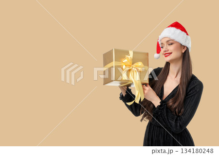 Smiling woman in a Christmas hat holds a gift box 134180248