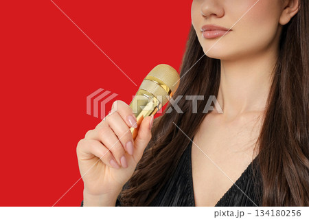 Close-up of a woman holding a gold microphone against vibrant red Close-up of a woman holding a gold microphone against vibrant red 134180256