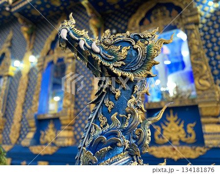 A detailed sculpture of a mythical guardian figure in vibrant blue and gold, showcasing ornate Thai craftsmanship with rich textures and cultural artistry 134181876
