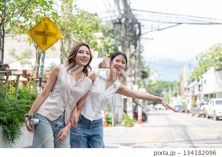 Pretty asian woman holding camera and friend calling taxi while standing on sidewalk by street road. 134182096