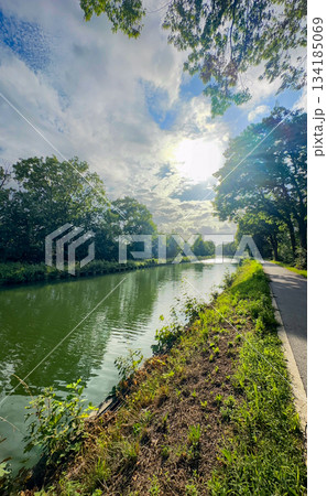 Idyllic riverside route with lush greenery and sparkling reflections Idyllic riverside route with lush greenery and sparkling reflections 134185069