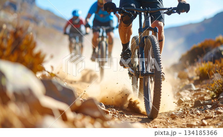 Mountain bikers riding through a dusty rocky trail in open wilderness, action outdoor cycling scene 134185366