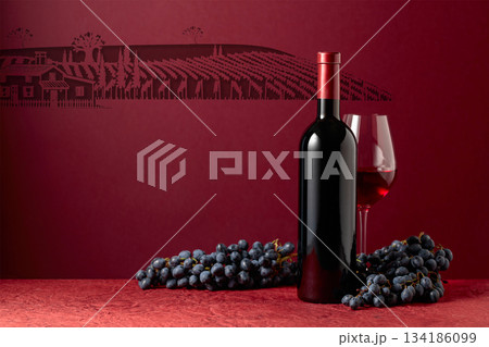 Bottle and glass of red wine with blue grapes on a red background. 134186099