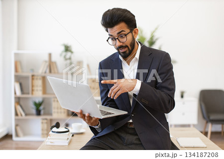 An Indian businessman is pointing at his laptop while working in an office setting 134187208