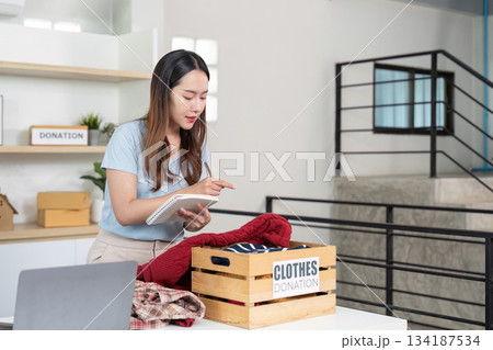 Clothes Donation. Young woman taking notes while organizing donations. 134187534