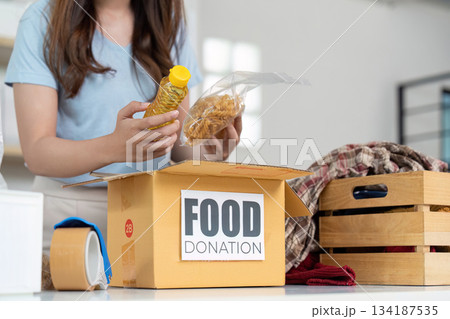 Food Donation. Woman preparing food items for charity in a cozy setting. Food Donation. Woman preparing food items for charity in a cozy setting. 134187535