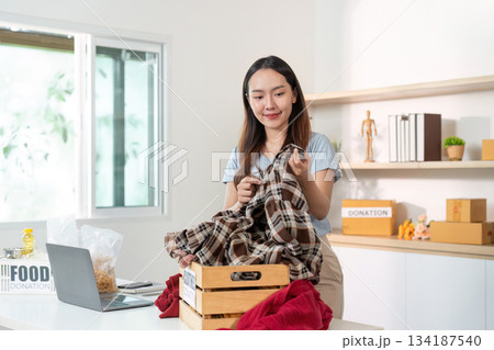Clothes Donation. Young woman organizing clothes for charity in a cozy space. 134187540