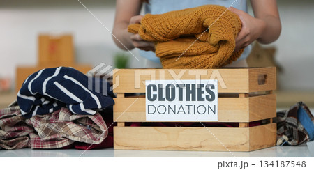 Clothes Donation. Individual placing warm sweater into donation box. 134187548
