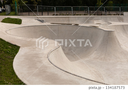 The skatepark features smooth, flowing curves and slopes, inviting skaters to enjoy the space. An open area under bright daylight enhances the welcoming atmosphere for fun activities The skatepark features smooth, flowing curves and slopes, inviting skaters to enjoy the space. An open area under bright daylight enhances the welcoming atmosphere for fun activities 134187573