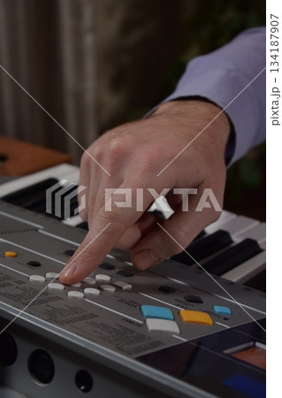 A young white man plays an electronic synthesizer indoors, immersed in his creative hobby. Focused on shaping tones and melodies, he explores musical expression and artistry in a calm home setting. 134187907