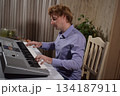 A young white man plays an electronic synthesizer indoors, immersed in his creative hobby. Focused on shaping tones and melodies, he explores musical expression and artistry in a calm home setting. 134187911
