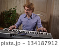 A young white man plays an electronic synthesizer indoors, immersed in his creative hobby. Focused on shaping tones and melodies, he explores musical expression and artistry in a calm home setting. 134187912