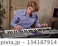 A young white man plays an electronic synthesizer indoors, immersed in his creative hobby. Focused on shaping tones and melodies, he explores musical expression and artistry in a calm home setting. 134187914