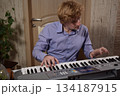 A young white man plays an electronic synthesizer indoors, immersed in his creative hobby. Focused on shaping tones and melodies, he explores musical expression and artistry in a calm home setting. 134187915