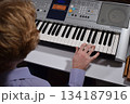 A young white man plays an electronic synthesizer indoors, immersed in his creative hobby. Focused on shaping tones and melodies, he explores musical expression and artistry in a calm home setting. 134187916
