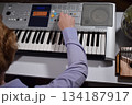 A young white man plays an electronic synthesizer indoors, immersed in his creative hobby. Focused on shaping tones and melodies, he explores musical expression and artistry in a calm home setting. 134187917