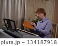 A young white man plays an electronic synthesizer indoors, immersed in his creative hobby. Focused on shaping tones and melodies, he explores musical expression and artistry in a calm home setting. 134187918