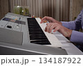 A young white man plays an electronic synthesizer indoors, immersed in his creative hobby. Focused on shaping tones and melodies, he explores musical expression and artistry in a calm home setting. 134187922