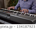 A young white man plays an electronic synthesizer indoors, immersed in his creative hobby. Focused on shaping tones and melodies, he explores musical expression and artistry in a calm home setting. 134187923
