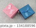 Two small boxes with ribbons are placed on a shiny surface. One box is blue and the other is pink. These boxes are ready for gifting during a party or event. 134188596