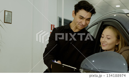 Car salesman handing keys to a happy female customer in the showroom Car salesman handing keys to a happy female customer in the showroom 134188974