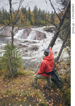 A tourist in a red jacket looks at a waterfall in an autumn forest A tourist in a red jacket looks at a waterfall in an autumn forest 134188987