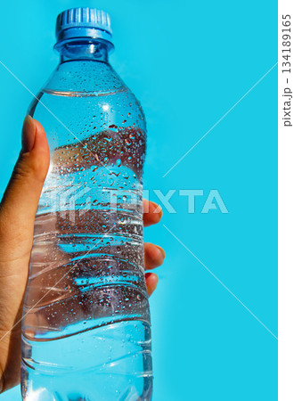 Hand holding water bottle over blue background. Still water bottle with water drops. 134189165