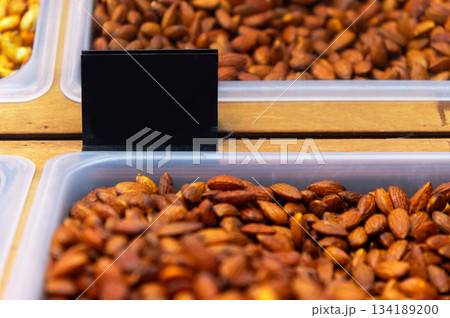 A black, blank price tag on a store counter next to a container of roasted almonds, shot with a shallow depth of field and soft focus. Price tag for roasted almonds 134189200