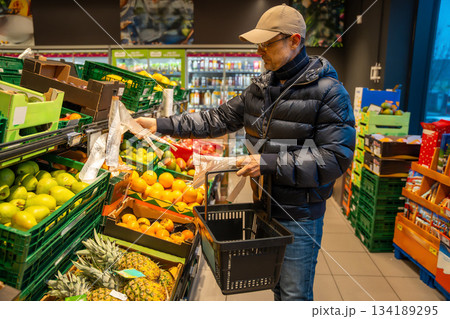 Man tearing off a plastic produce bag at a fresh fruit and vegetable section in a supermarket. Raises awareness about single use plastic consumption in daily grocery shopping. 134189295