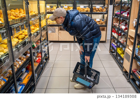 Man choosing fresh pastry in the bakery section of a supermarket. Depicts conscious food selection and daily grocery shopping habits. 134189308