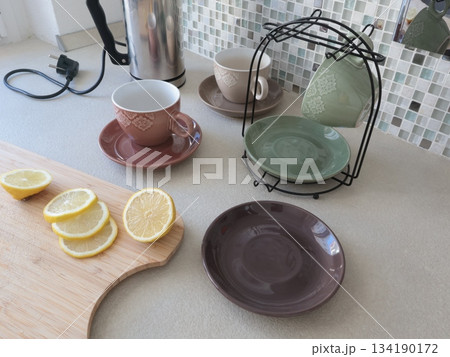 Ceramic cups and sliced lemon on wooden cutting board. Tea and cooking in kitchen. Food and drinks. Set of dishes on stand. Ceramic cups and sliced lemon on wooden cutting board. Tea and cooking in kitchen. Food and drinks. Set of dishes on stand. 134190172