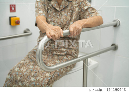 Asian elderly woman patient use toilet support rail in bathroom. 134190448