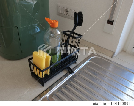 Black stand with cleaning agent, brush and sponge in kitchen near sink. Cleanliness in house. Care and cleaning. Black stand with cleaning agent, brush and sponge in kitchen near sink. Cleanliness in house. Care and cleaning. 134190892