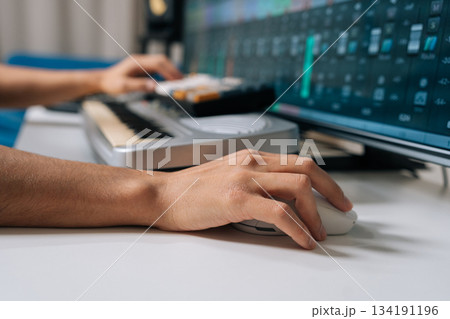 Hands manipulating synthesizer midi keyboard and computer keyboard while controlling daw on screen with faders and tracks, composing and mixing music in modern home studio, close-up. 134191196