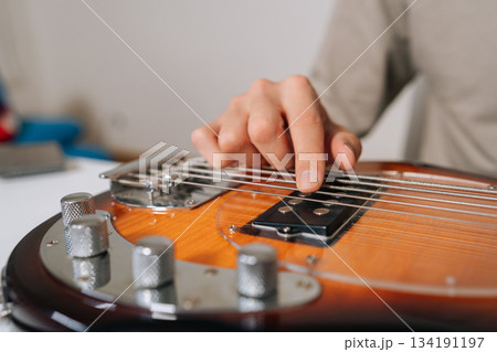 Close-up of musician hand plucking and adjusting bass guitar strings, preparing and tuning instrument for practice, rehearsal or live performance with focused precision. 134191197