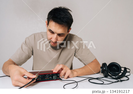 Portrait of audio engineer male holding red usb audio interface card and plugging cable into headphone output, setting up for music creation, sound recording, and mixing in home studio. 134191217