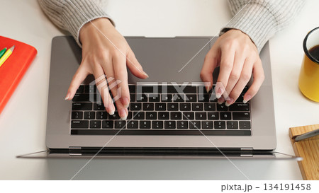 Top view of woman's hands typing on laptop keyboard, representing work, AI prompt, research, social networks, and remote education in a modern workspace. Top view of woman's hands typing on laptop keyboard, representing work, AI prompt, research, social networks, and remote education in a modern workspace. 134191458