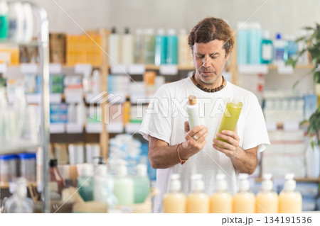 man chooses a dandruff shampoo at the pharmacy 134191536